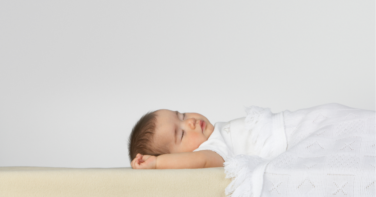 Baby sleeping peacefully with a soft blanket and sound machine nearby.